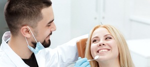 A woman smiling at her dentist while he checks her cosmetic dental bonding