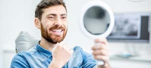 dental patient admiring his new smile in a mirror 
